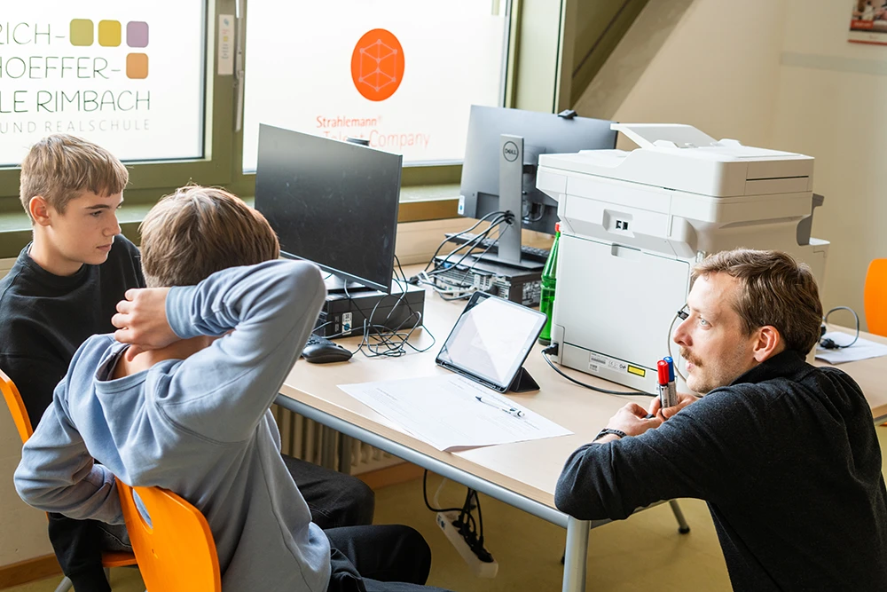 Lehrer mit Schülern im Dialog - Schüler am Schreibtisch